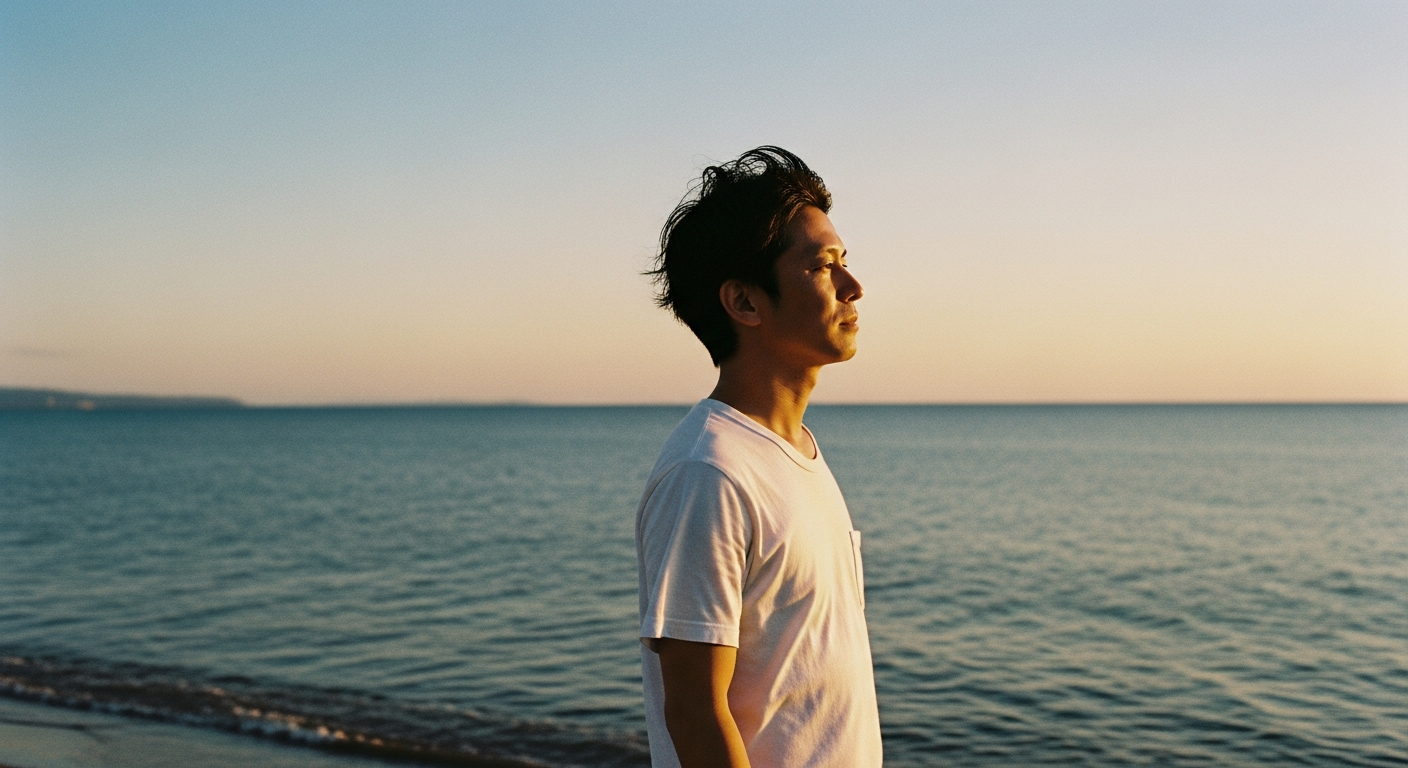 Japanese man standing on beach looking at the ocean